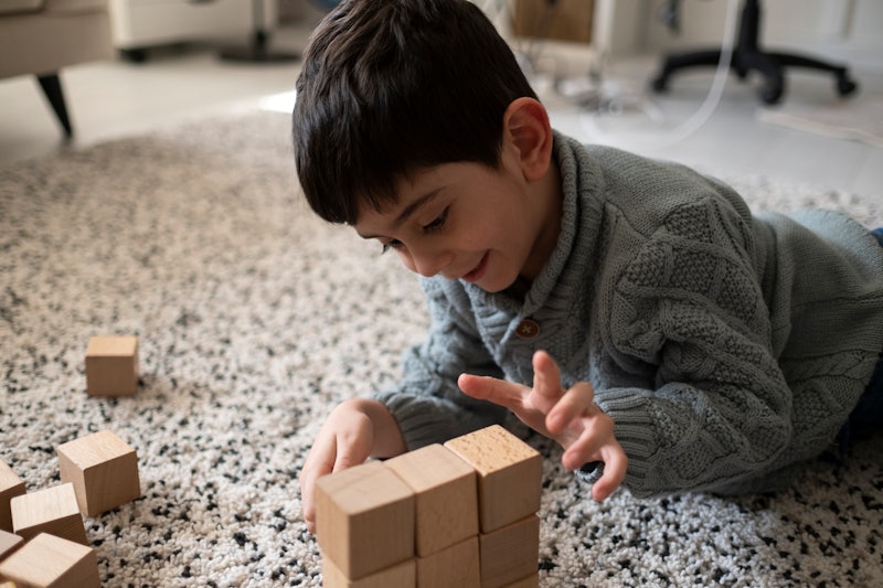 Little child sitting on the floor. Pretty boy palying with wooden cubes at home