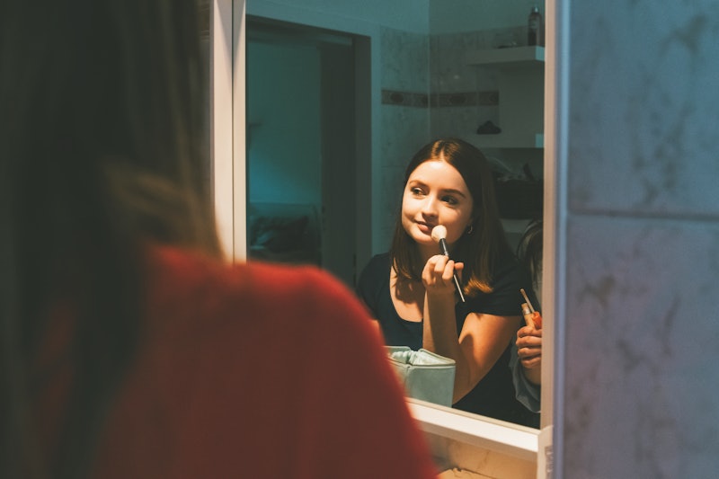 young woman putting up make up in front of mirror in bath room