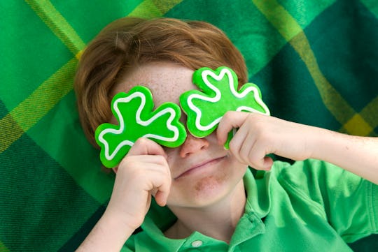 Redhead and freckle face Irish boy leprechaun with shamrock cookies over his eyes. Smiling Irish chi...