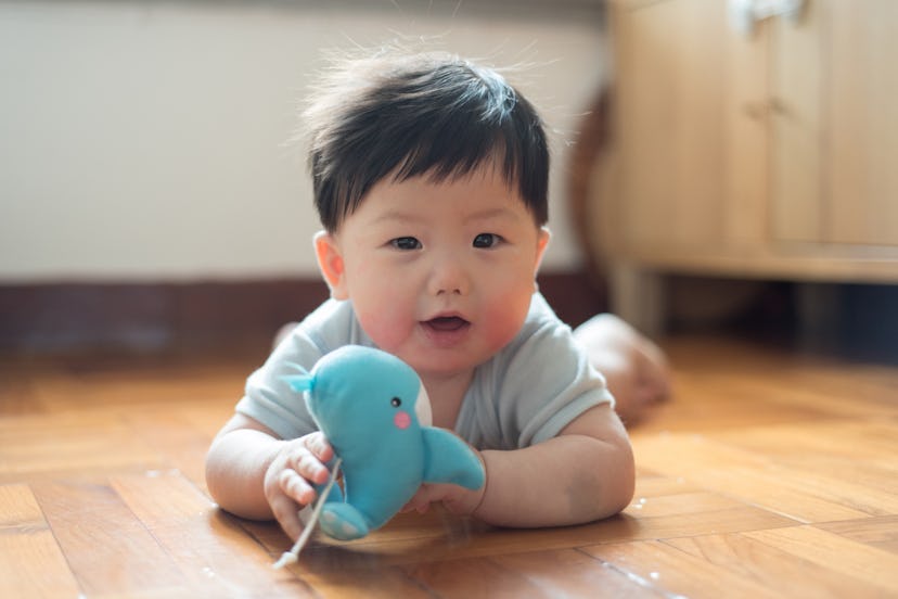 7 months old baby boy playing toy whale while lying on wooden floor