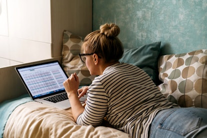 woman working on her bed, doing taxes on laptop