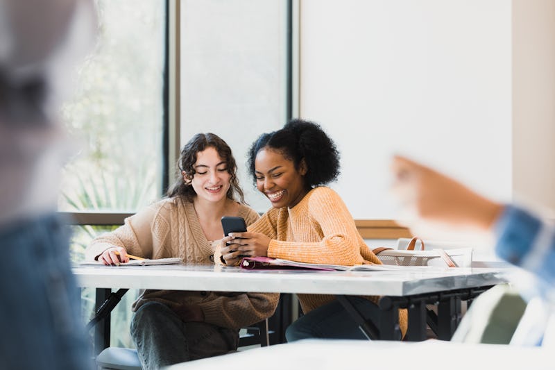 The female classmates look at their phones laughing at a funny picture they saw.