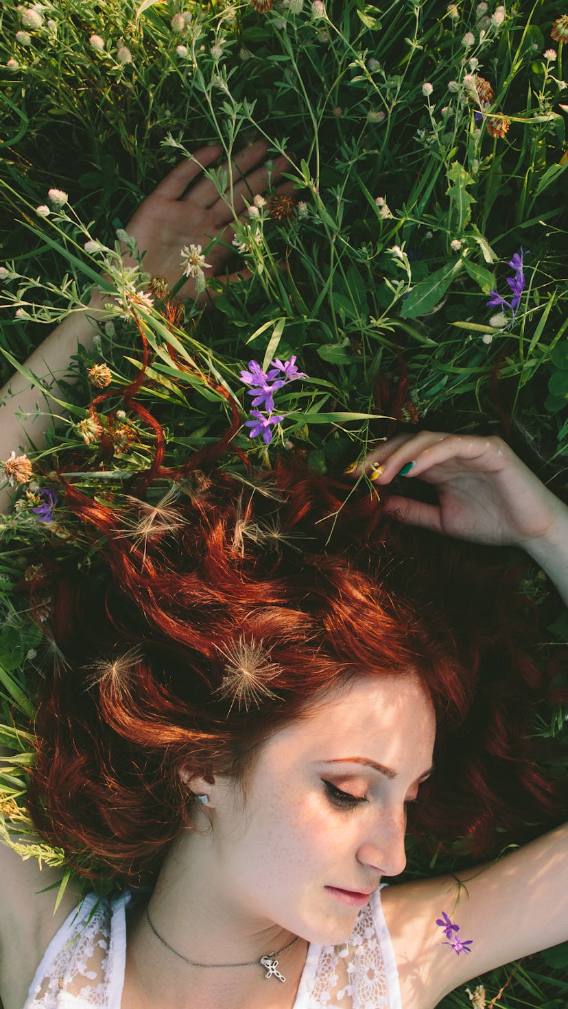 A young red-haired woman with a spring wreath lies on the field grass, resting, smiling. Aries seaso...