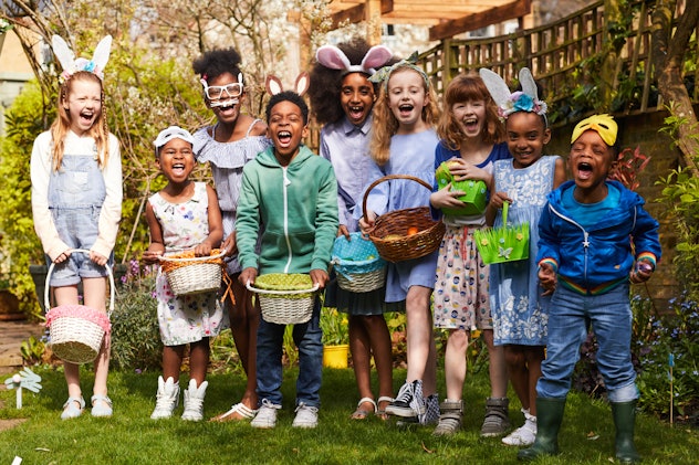 Group of children having fun on an Easter Egg Hunt, laughing and shouting, outside in the sun.