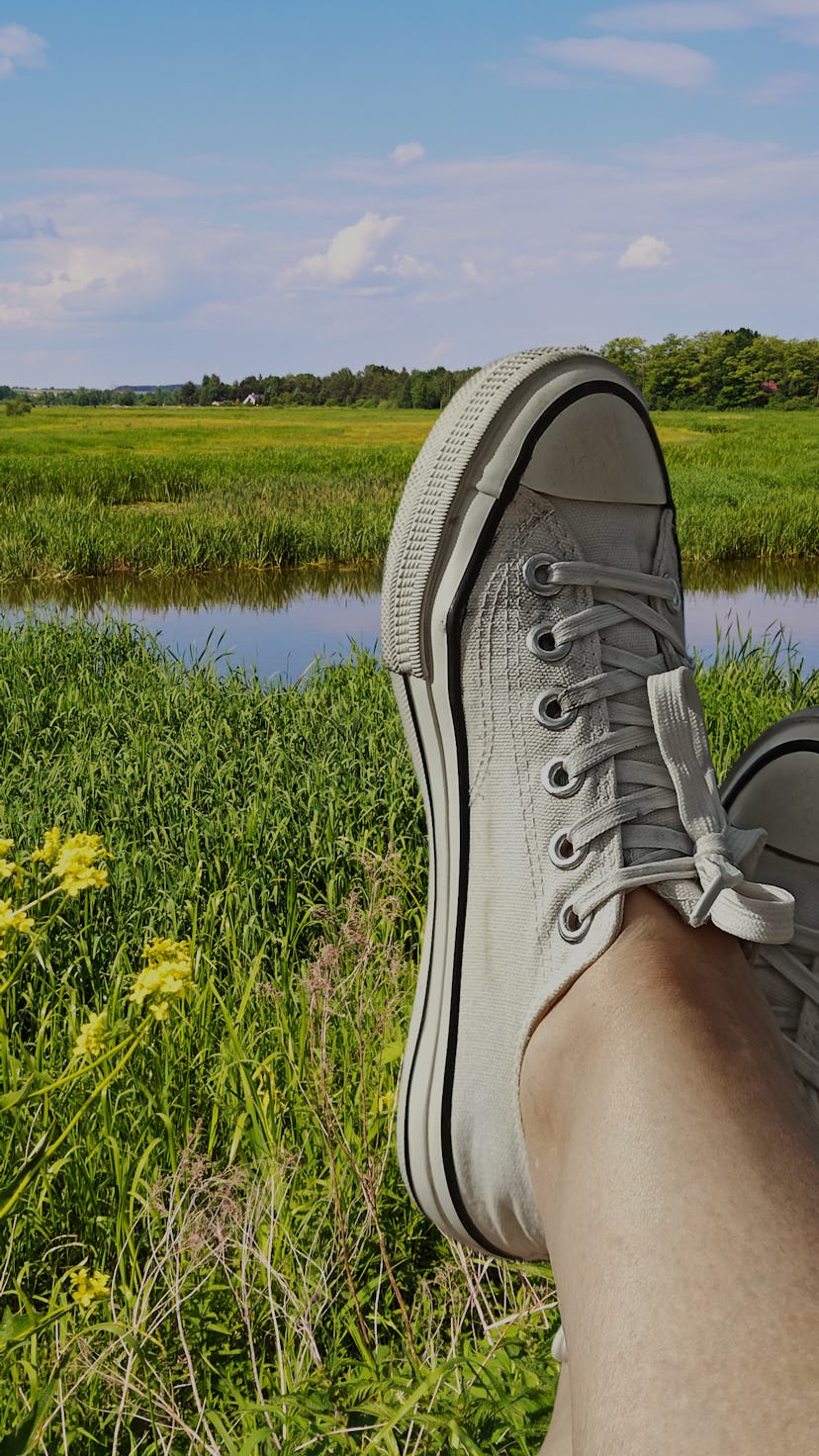 Close-up of female legs in white sneakers on the background of nature.