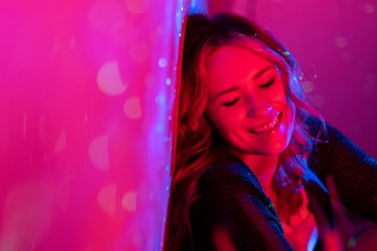Young woman smiling under neon lighting, knowing her zodiac sign will have the best week of March 28...