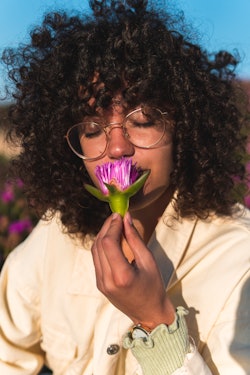 A woman smells a purple flower. These are the personality traits of a pisces-aries cusp.