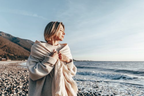 A woman cuddles in a blanket near the beach. Here's your daily horoscope for March 21, 2022.