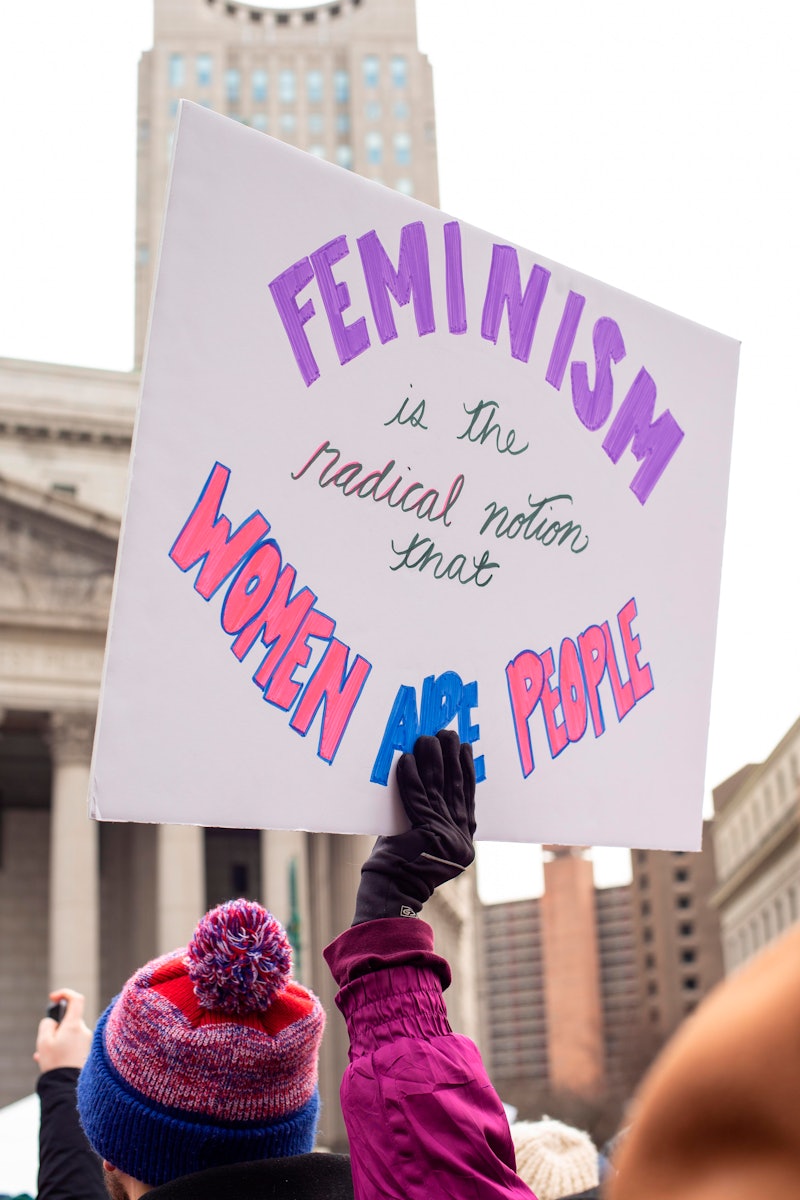 A woman holds a feminist protest sign. Women's charities to donate to during women's month.