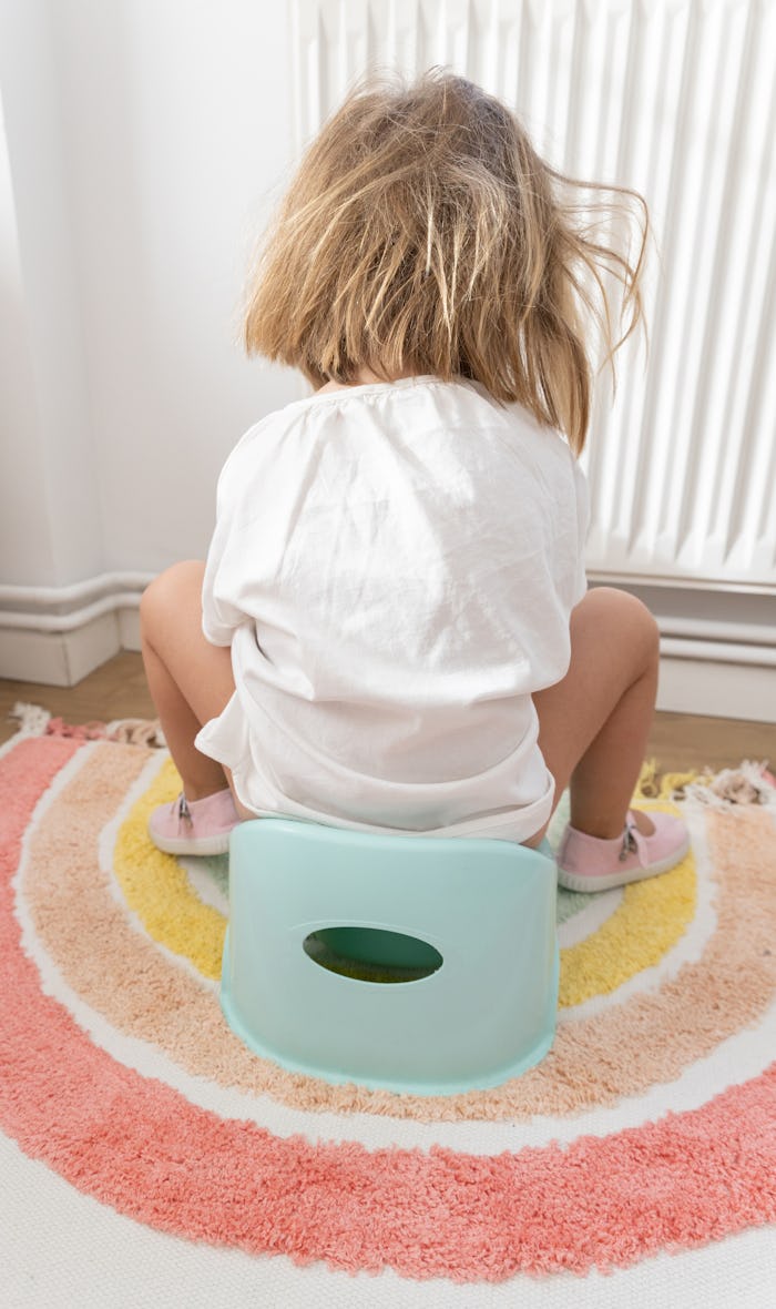 girl sitting on training potty seat reading a potty training book