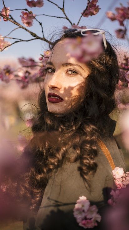 Young woman surrounded by flowers reflects on the 2022 pink moon, which will affect every zodiac sig...