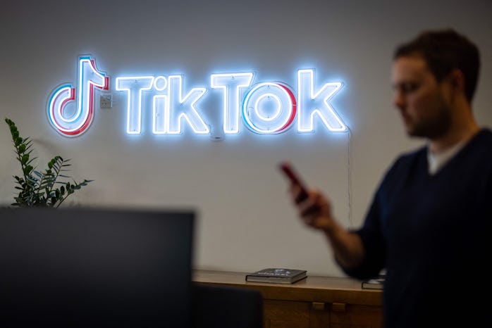 An employee looks at his mobile phone as he walks past the logo of the video-focused social networki...