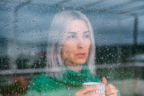 A woman watches the rain through a window. Here's your daily horoscope for today: March 22, 2022.