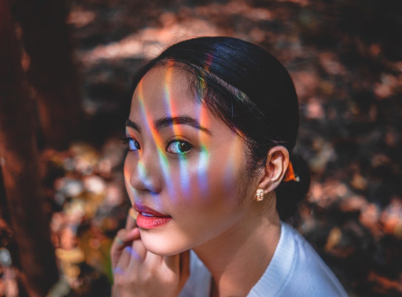 Woman wearing sunscreen under makeup looking into the sun with rainbows on her face