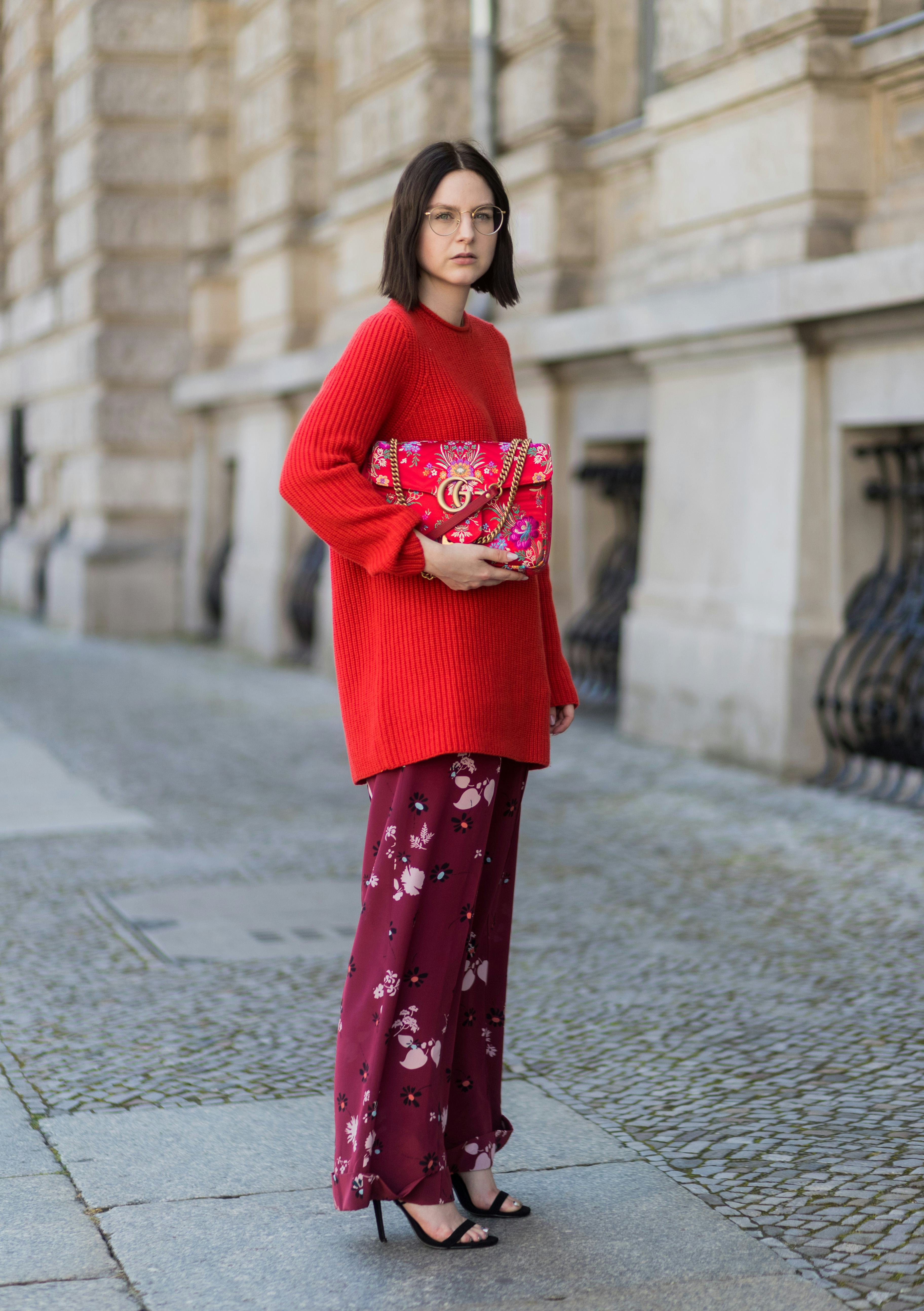 A model wearing red and a floral bag.