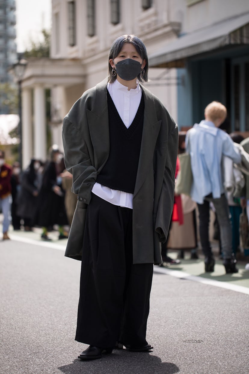 TOKYO, JAPAN - MARCH 19: A guest is seen wearing oversize outfit with grey coat, black sweater vest,...