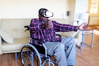 Cheerful Disabled Senior Afro-American Man, in a Wheelchair, is Gesturing and Smiling, While Wearing...