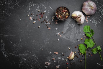 Close up of traditional cooking ingredients: garlic, olive oil, salt, pepper, fresh herbs on dark ru...