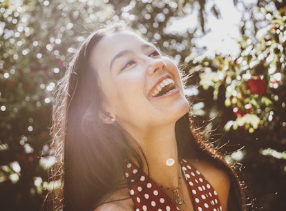 Young woman laughing in a beautiful garden, knowing her lucky zodiac sign will have the best month o...
