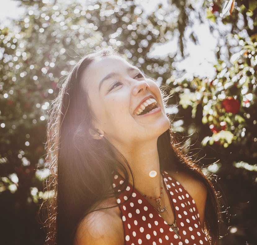 Young woman laughing in a beautiful garden, knowing her lucky zodiac sign will have the best month o...