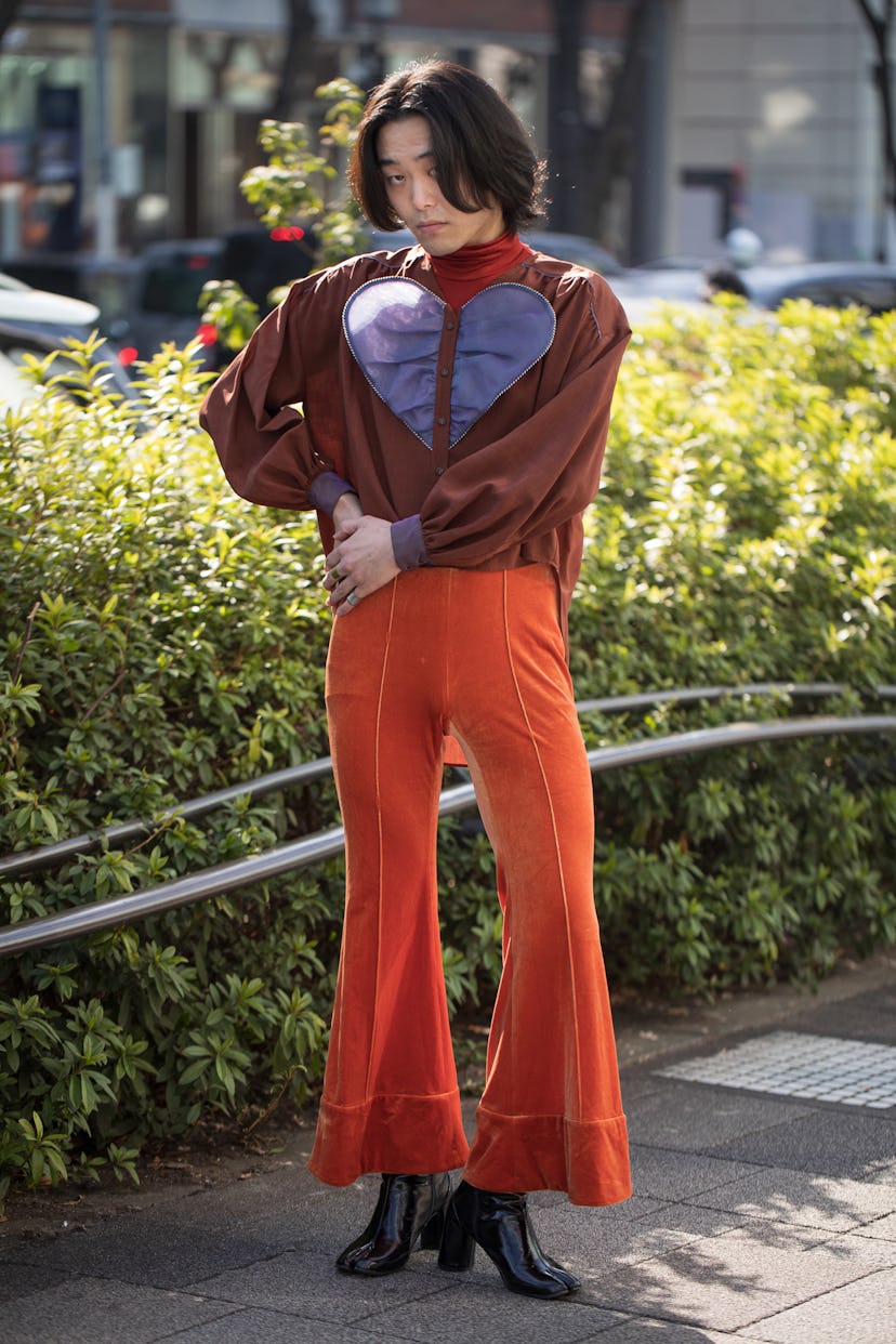 TOKYO, JAPAN - MARCH 15: A guest is seen wearing orange flared pants, brown with purple heart design...