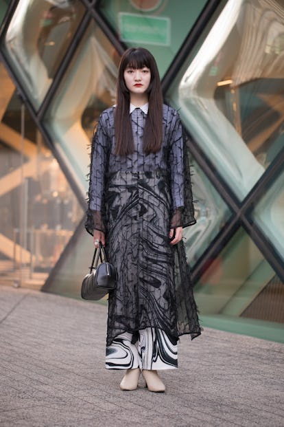 TOKYO, JAPAN - MARCH 15: A guest is see wearing sheer black dress, black/white print skirt, taupe sh...