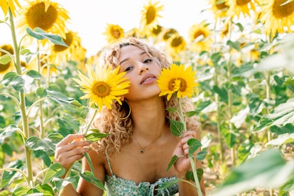 Young woman standing in a sunflower field, knowing her lucky zodiac sign will have the best month of...
