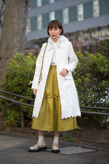 TOKYO, JAPAN - MARCH 15: A guest is seen wearing white coat, olive skirt, colorful print shoes outsi...