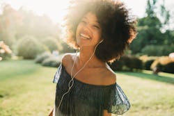 A woman with wired headphones smiles in a park. Here's your daily horoscope for today, March 23, 202...