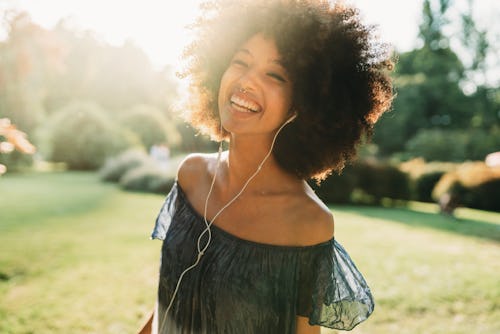 A woman with wired headphones smiles in a park. Here's your daily horoscope for today, March 23, 202...