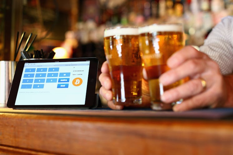 A terminal to accept payments using bitcoins on a bar and a person putting down two beer jugs