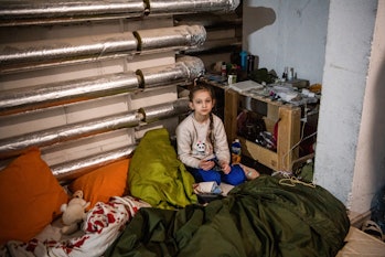 KYIV, UKRAINE - 2022/03/21: A girl sits on a makeshift bed in a basement near the blast that destroy...