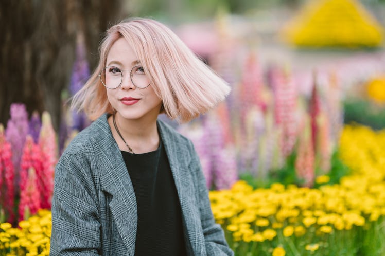 Young woman with pink hair standing in front of spring flowers, embracing the April 2022 monthly hor...