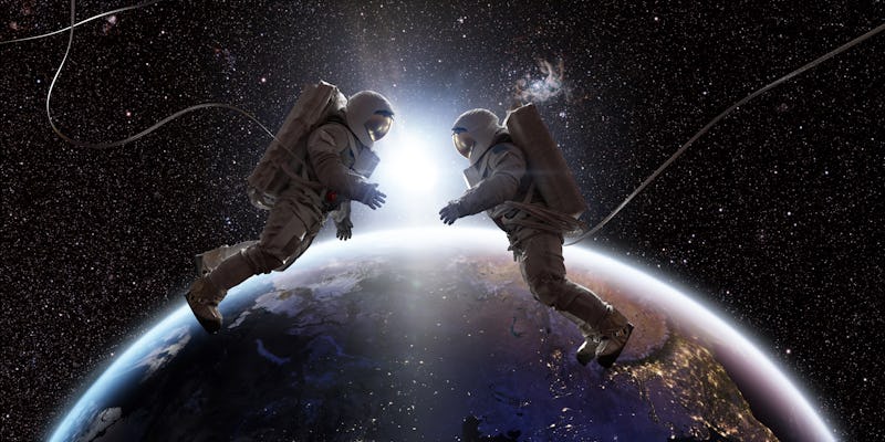 Two astronauts in full spacesuits with backpacks on a space walk with tethers, facing each other wit...