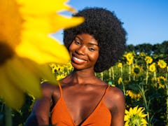 Young woman smiling in a field of sunflowers, knowing her zodiac sign will be affected by the April ...