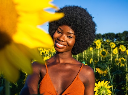 Young woman smiling in a field of sunflowers, knowing her zodiac sign will be affected by the April ...