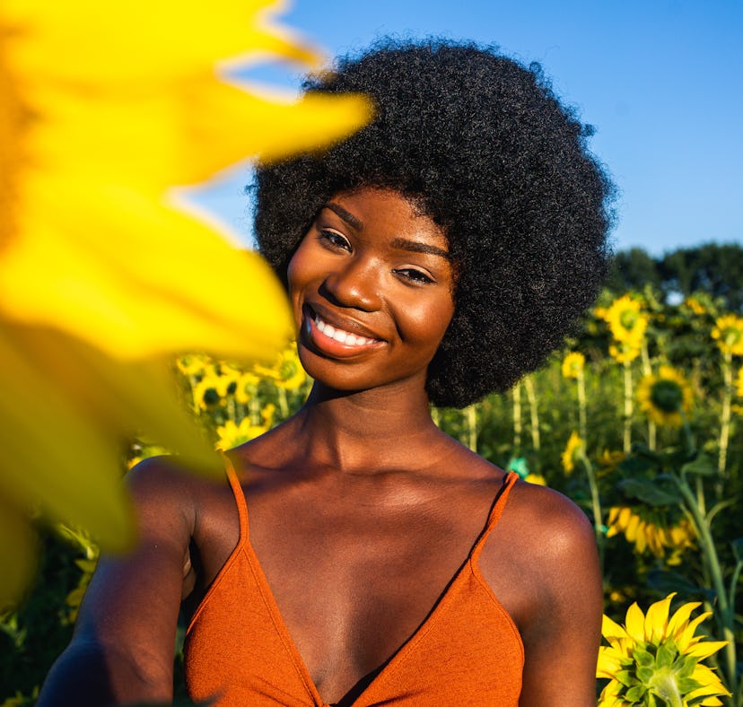 Young woman smiling in a field of sunflowers, knowing her zodiac sign will be affected by the April ...