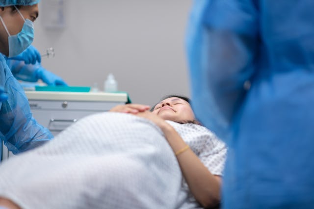 A pregnant woman is going in to surgery. She is laying on an operating table in the hospital's opera...