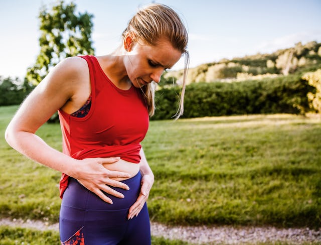 Sporty woman outdoors, holding her stomach in pain