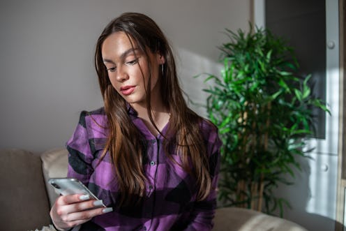 A young woman is sitting on a sofa and using a mobile phone