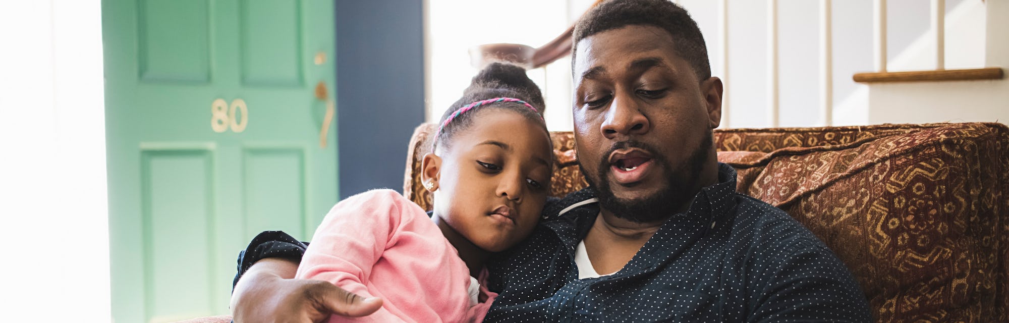 father and daughter reading book together on couch