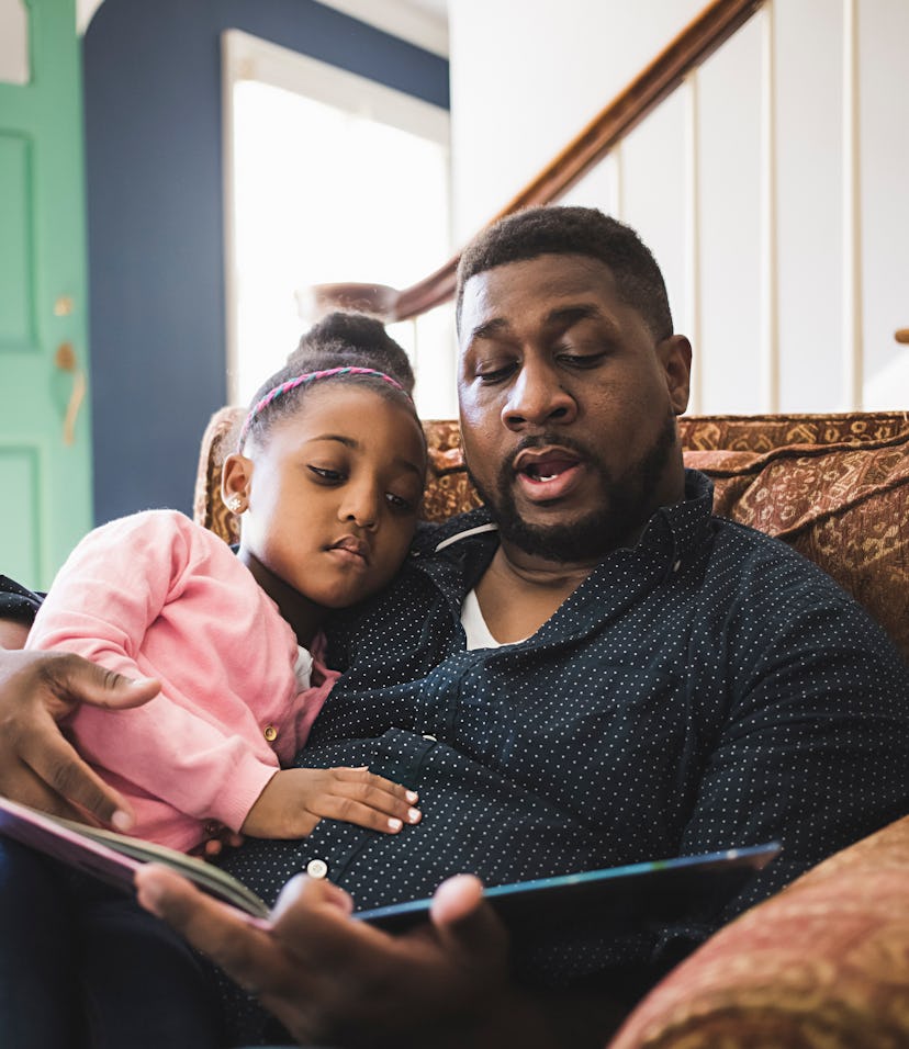 father and daughter reading book together on couch