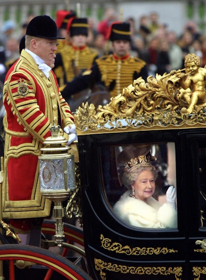 Queen Elizabeth II waves to the crowd from her horse carriage under the watchful eye of her footman ...
