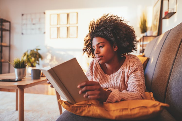 A woman at home reads one of the spring break reads on this list.