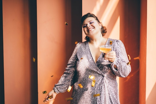 Smiling woman holding champagne glass and throwing confetti.