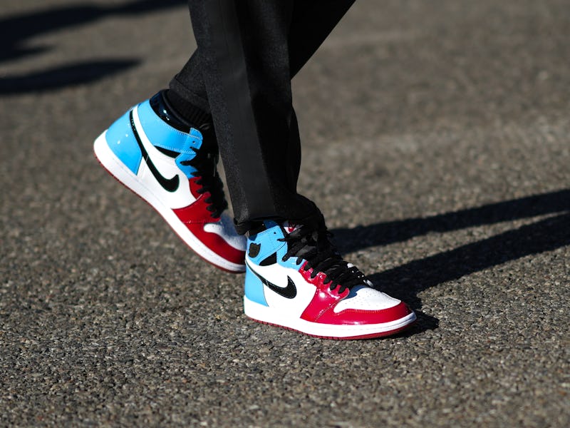 MILAN, ITALY - FEBRUARY 23: A guest wears black suit pants, a white / blue / red shiny leather ankle...