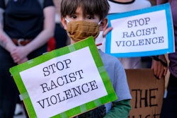 A boy wearing a face mask and holding a sign reading "Stop Racism Violence" takes part in a rally in...