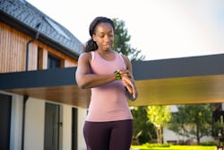 Smiling mid adult woman checking the time on her wrist watch outside the house. What muscles does wa...