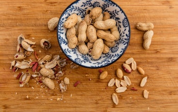 Peanuts in a bowl. Wooden board with peanut shells, cotelydons and seed coats.