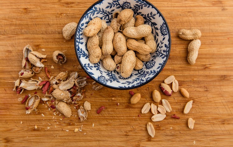 Peanuts in a bowl. Wooden board with peanut shells, cotelydons and seed coats.